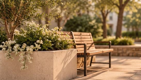 A wooden bench beside a stone planter of white flowers in warm evening light